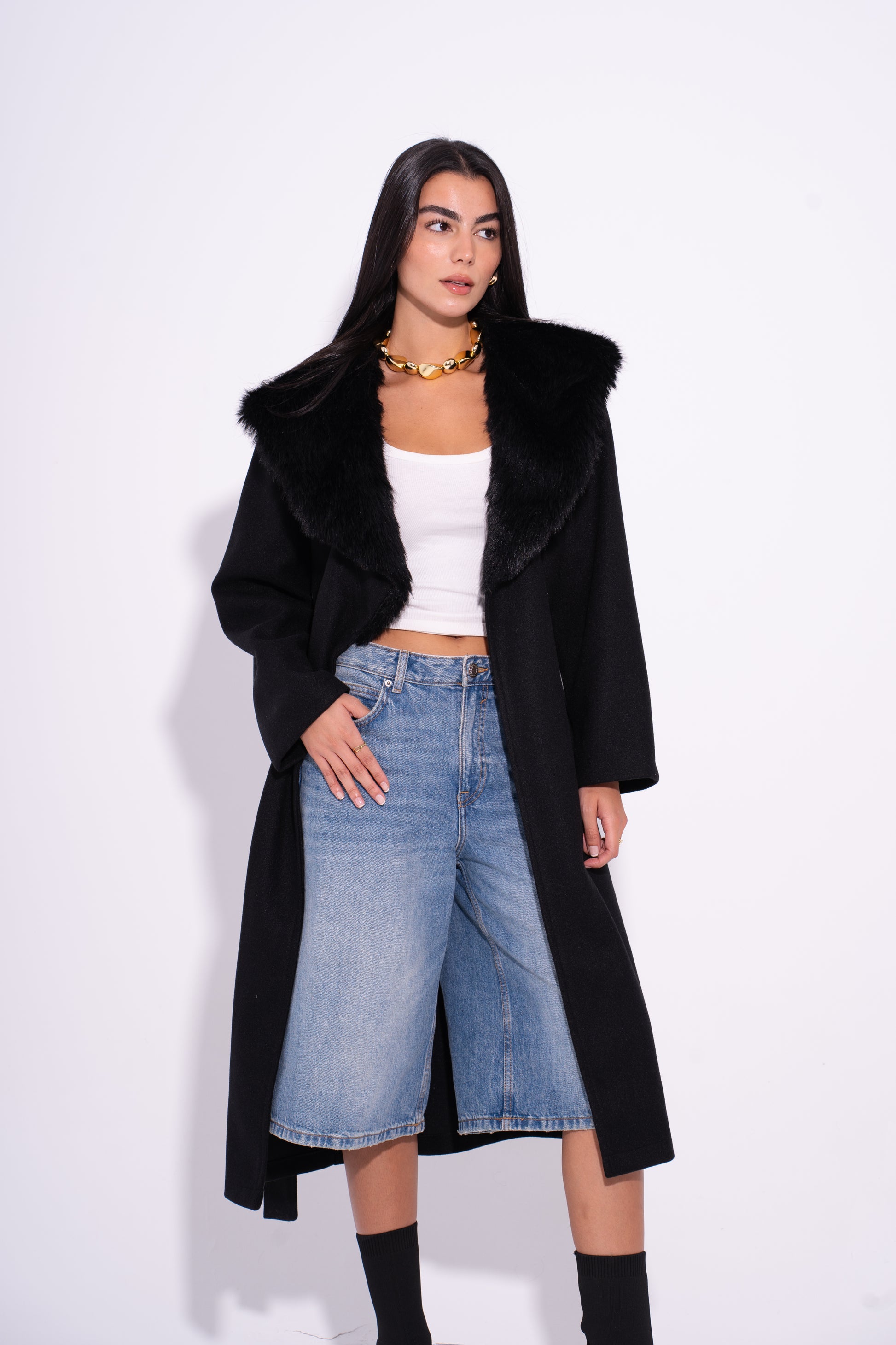 Woman wearing a black coat, white top, and blue jeans on a white background